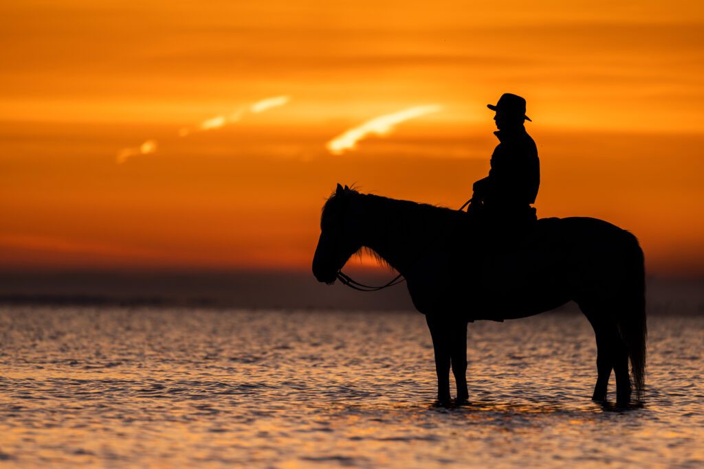 A man riding a horse in the water at sunset, named "Being in the Moment".